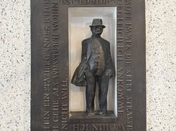 Ein Mann mit Hut steht in einer Nische, umgeben von deutschen Texten.