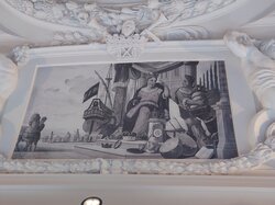 Ein monochromes Kunstwerk zeigt eine sitzende Figur, umgeben von verschiedenen Gegenständen, mit einem Schiff und Menschen im Hintergrund.