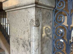 Eine Marmorsäule mit kunstvollen Schnitzereien steht neben einem dekorativen Metallgitter.