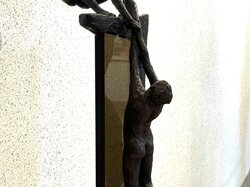 Zwei Bronzefiguren auf einem Sockel, von denen die eine nach oben reicht und die andere nach unten hängt.