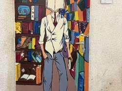 Ein Mann in weißem Hemd und blauer Jeans steht vor einem bunten Bücherregal.