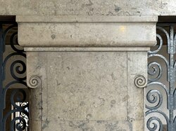 Eine Steinsäule mit kunstvollen Schnitzereien steht neben einem dekorativen schmiedeeisernen Tor.