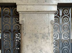 Eine Säule mit verschlungenen Spiralen steht neben einem dekorativen schmiedeeisernen Zaun.