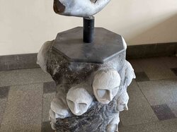 Eine skulpturale Arbeit mit mehreren Gesichtern, einer Hand und einem kreisförmigen Spiegel auf der Oberseite.