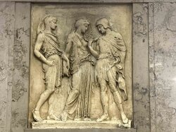 Drei Figuren in klassischer Kleidung sind in einem Flachrelief dargestellt.