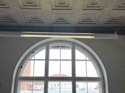 Ein Raum mit einem geometrischen Deckenmuster, einem großen Rundbogenfenster und einer Wandleuchte.