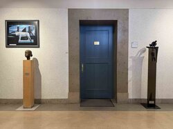 Kunstwerke, die in einem Raum mit einer blauen Tür ausgestellt sind.